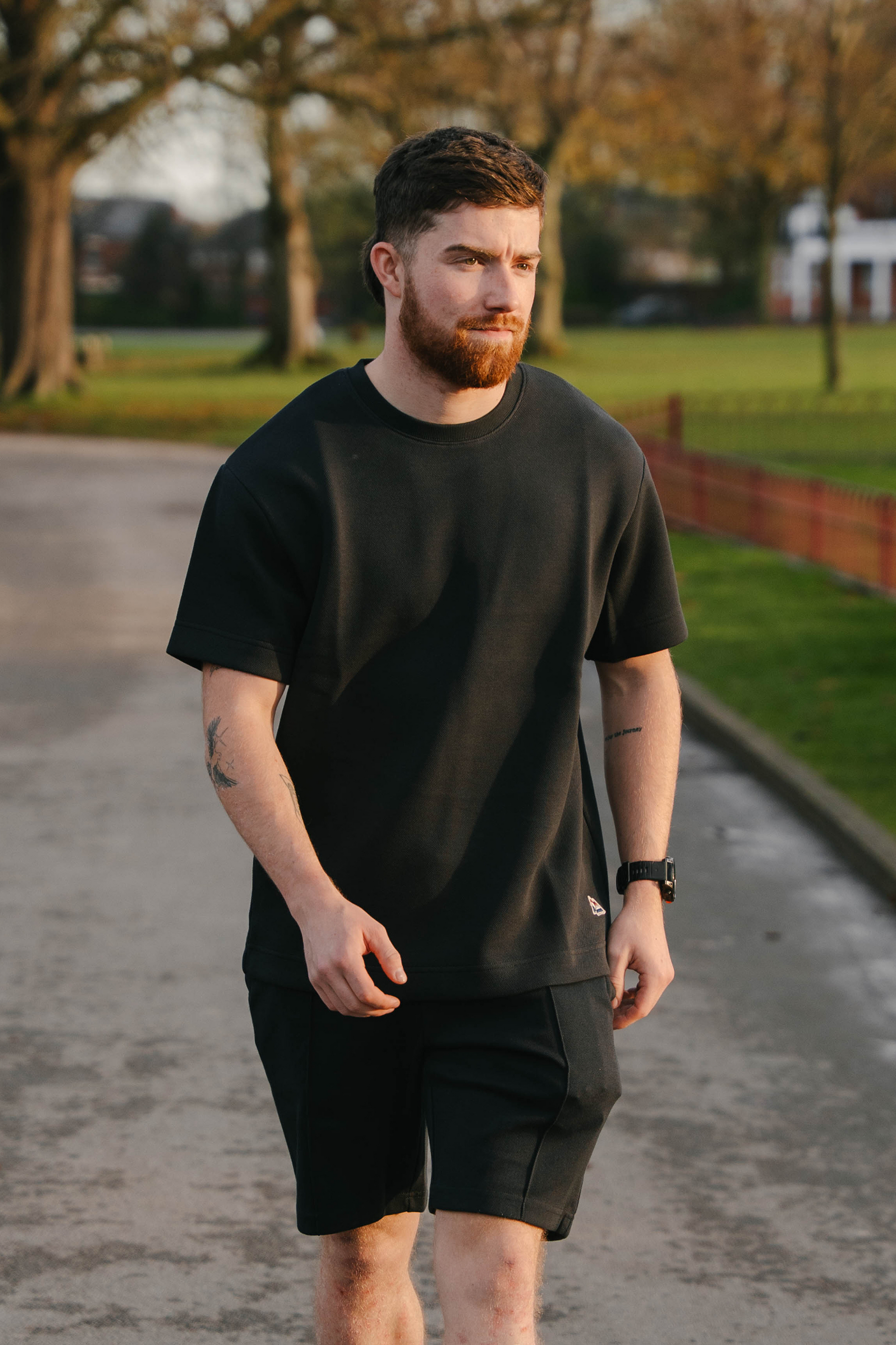 Man wearing a black t-shirt and shorts walking on a path with trees and grass in the background