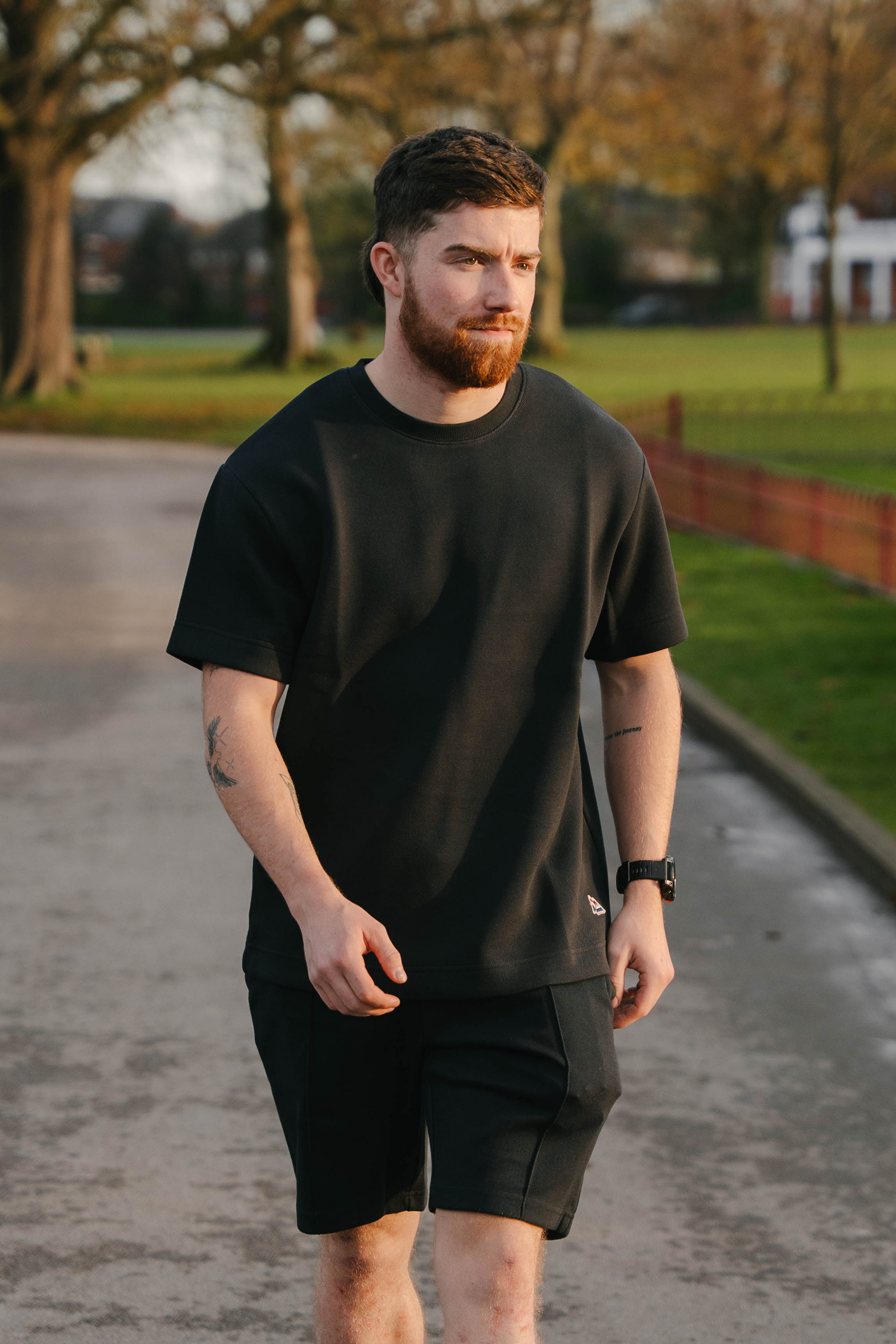 Man wearing a black t-shirt and shorts walking on a path with trees and grass in the background